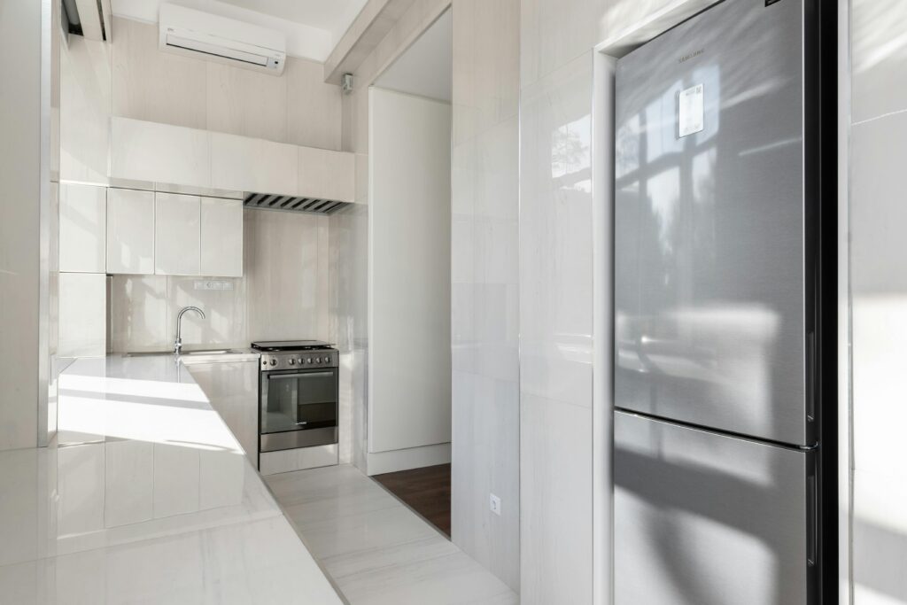 Completely empty kitchen with white counters and a modern fridge. The best move-out cleaning services in Lakewood